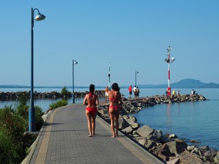 Obraz premium Balatonmáriafürdő, Hungary - July 30, 2020: Bronzed women in red bikinis walking on the pier at the lake Balaton in a hot summer day in Hungary