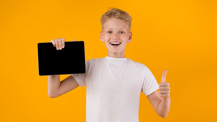 Smiling school boy showing tablet screen and thumbs up