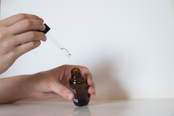 Manos sujetando un gotero y un pequeño bote de cristal sobre fondo blanco