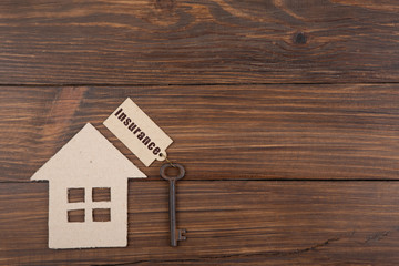 Insurance - text on the key label. House model and old key on wooden background real estate buy or rent concept