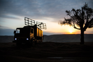 Fototapeta premium Silhouette of mobile air defence truck with radar antenna during sunset. Satellite dishes or radio antennas against evening sky.