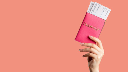 Passport control. Global immigration. Female hand holding foreign id in pink cover first class flight ticket isolated on coral copy space background. Vacation tour. Holiday trip. - obrazy, fototapety, plakaty