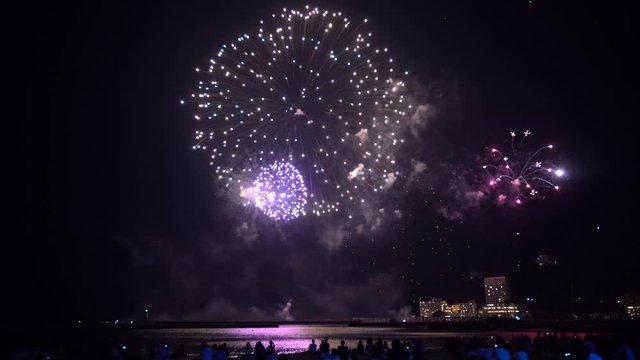 Silhouettes of crowds of people enjoying summer fireworks in front of Ocean at night