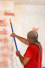 a man with a paint roller applies a primer to the wall