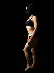 adult caucasian appearance woman in a black bra and bikini stands on a black background