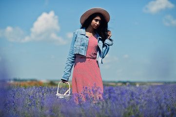 Beautiful indian girl in summer dress and jeans jacket in purple lavender field with basket in hand...