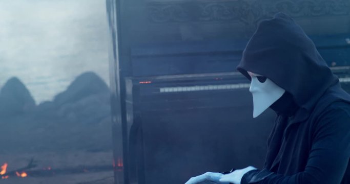 a man in a venetian mask on the sunrise plays the glucophone against the background of a burning old piano