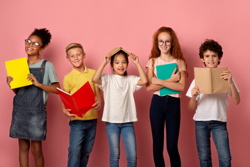 School education. Portrait of smiling diverse kids with books and copybooks looking at camera, pink background - Powered by Adobe