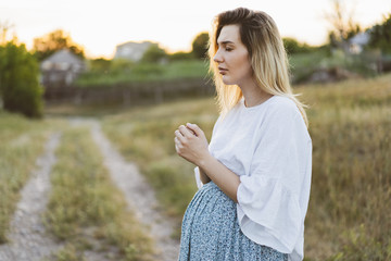 Pregnant woman praying outdoors on at sunset. Concept for faith, spirituality and religion. 