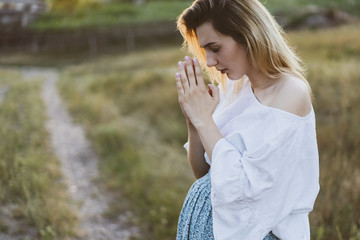 Pregnant woman praying outdoors on at sunset. Concept for faith, spirituality and religion. 