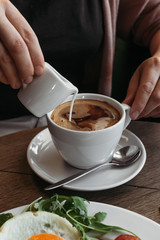 Girl in cafe pours milk into an espresso.