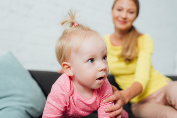 Selective focus of woman touching excited baby girl on couch