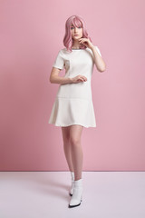 Beautiful girl with pink hair, hair coloring. Cute anime woman stands on a pink background in a short white dress. Colored hair, perfect hairstyle
