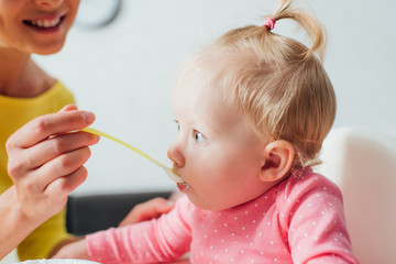 Fototapeta premium Selective focus of woman feeding daughter with baby food at home