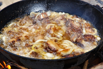 Pieces of lamb with onion are fried in boiling oil on the fire. As a stage in the preparation of traditional pilaf.