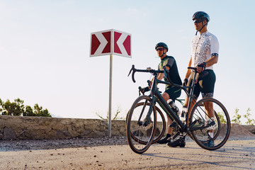 Two male cyclists stand on the road and have a rest