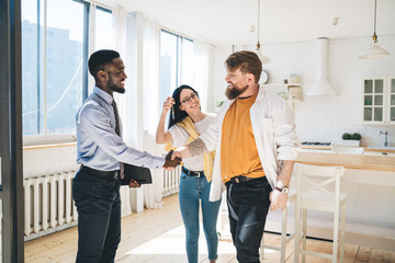 Black realtor and happy couple sealing deal by shaking hands