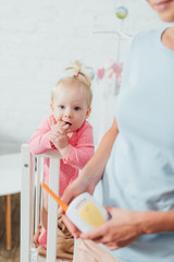 Fototapeta premium Selective focus of infant in crib near mother holding baby monitor