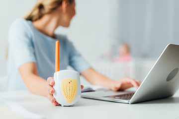 Selective focus of woman using laptop and holding baby monitor at home