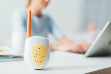 Selective focus of baby monitor on table and woman using laptop at home