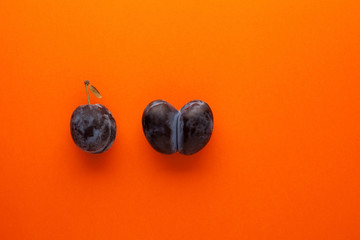 Ripe plum and ugly accreted prunes on an orange background. Place for text. Fused fruits. Funny,...