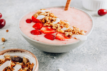 Healthy banana and strawberrie smoothie in a bowl with pieces of strawberries, granola and coconut chips