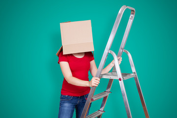 Person with cardboard box on its head standing behind a ladder on turquoise background