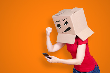 Person with cardboard box on its head and an angry face expression raising the fist against the smartphone on orange background