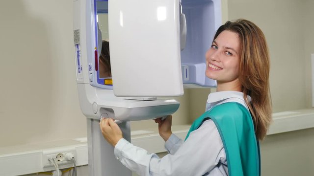 Portrait of young smiling woman near X-ray machine scanner. Equipment in modern dental clinic. Dental scanning. Computer 3d tomography of teeth and jaw. Healthcare concept. hd