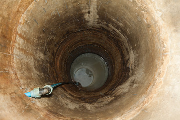 Wnętrze starej studni, zbudowanej z betonowych kręgów, z przyłączem do wody. Widok z góry.