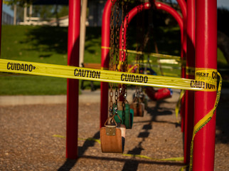 Empty saddle style swings at a playground covered in yellow caution tape written in english and...