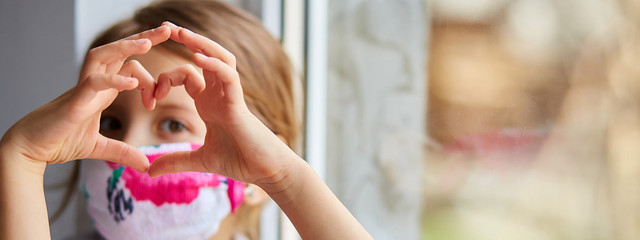 Little girl, child in mask making hearts from hands, coronavirus quarantine