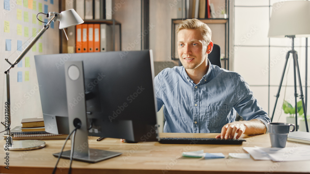 Poster creative entrepreneur sitting at his desk works on desktop computer in the stylish office. handsome 