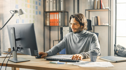Creative Entrepreneur Sitting at His Desk Works on Desktop Computer in the Stylish Office. Handsome Long Haired Hispanic Man with Artistic Look Uses Computer