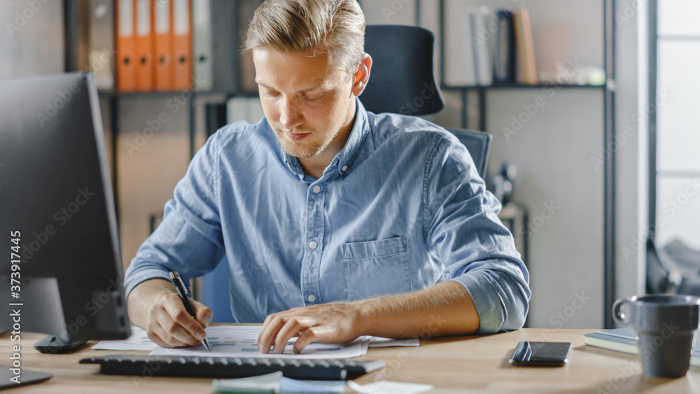 Poster handsome blonde businessman sitting at his desk in the office works on desktop computer, working wit