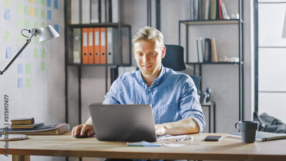 Poster handsome blonde businessman sitting at his desk in the office works on a laptop. creative entreprene