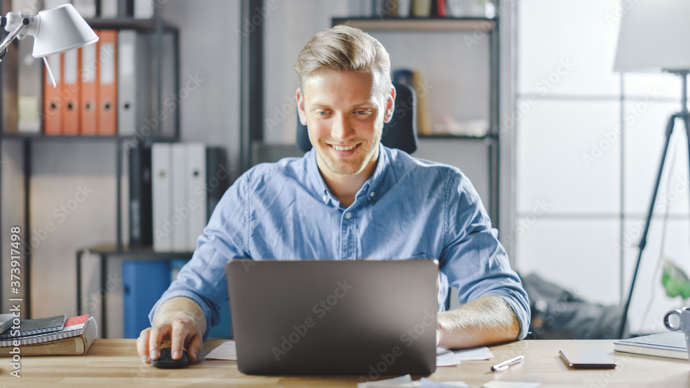 Poster handsome blonde businessman sitting at his desk in the office works on a laptop. creative entreprene
