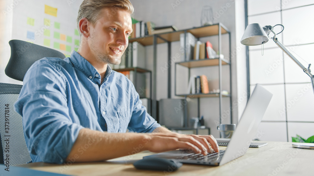 Poster handsome blonde businessman sitting at his desk in the office works on a laptop. creative entreprene