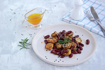 Warm salad of grilled Jerusalem artichoke and boiled red beans with olive oil and vinegar dressing on a white clay plate.
