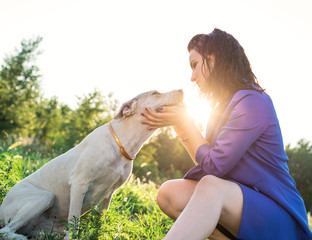 young attractive woman hugging her dog in the park in the sunset