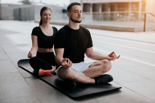 young couple handsome brunette man and beautiful woman in sportswear practicing yoga on mat on the street , relaxation , street workout, healthy fit lifestyle