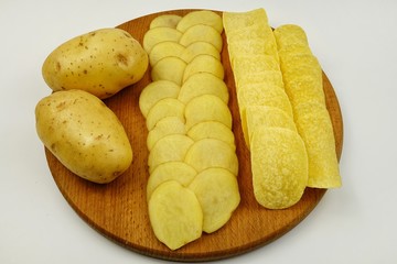 Raw potato tubers, raw potato slices and potato chips lie on a wooden board