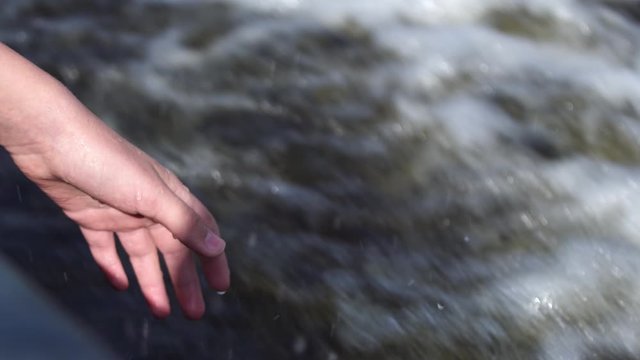 Closeup view of one young kids hand touching water while enjoying trip by motor boat. 4k video footage of motorboat water traces in blue river. 