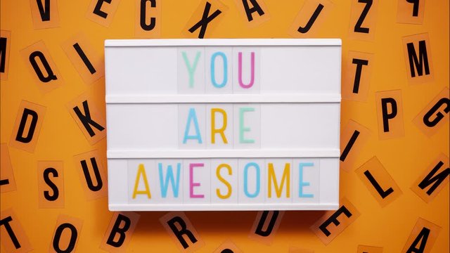 YOU ARE AWESOME sign on a letter board with letters being animated around. Orange background.