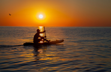 Silhouette of a man floating on a board with an oar. Dawn sun on the sea. Swimming on a supboard. Water active sports. Beautiful landscape. Sunset on the sea. Ocean coast. Copy space.