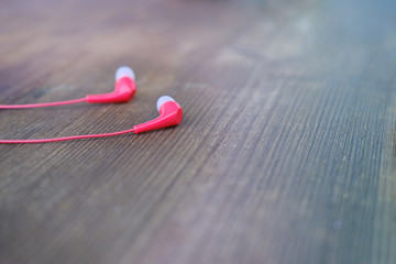 small red wired headphones lie on a vintage wooden table, blurred background, music harmony...