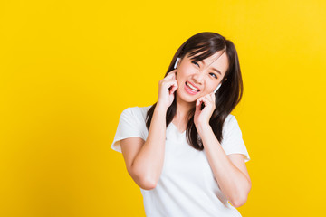 Portrait Asian of a happy beautiful young woman wear wireless earphone listening to music from smartphone having fun and dancing to sounds of favorite music studio shot isolated on yellow background