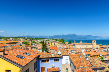 Fototapeta na wymiar Aerial panoramic view of Desenzano del Garda town with bell tower of Duomo di Santa Maria Maddalena Cathedral church, red tiled roof buildings, Garda Lake, mountain range, Lombardy, Northern Italy