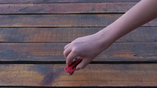 Kid playing with small toy car on wooden vintage background. Closeup view 4k video of boy hand holding small red toy car and other child attacks it with big plastic truck.