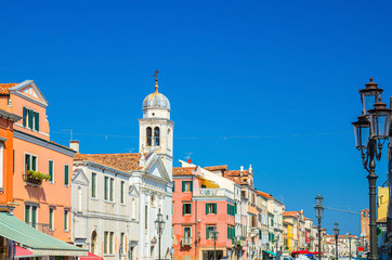 Fototapeta na wymiar Chiesa di San Francesco catholic church and row of colorful multicolored buildings in Chioggia town historical centre, blue sky background in summer day, Veneto Region, Northern Italy
